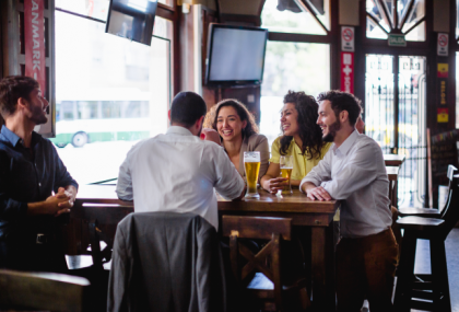 Two women and three men are sitting at a table in a pub, talking and enjoying beer.