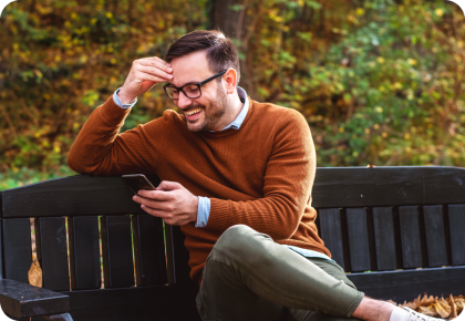 Man looking at phone and smiling on park bench