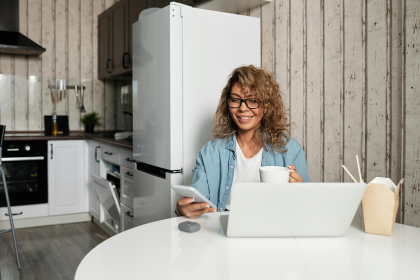 Woman sitting in a kitchen with laptop and mobile phone